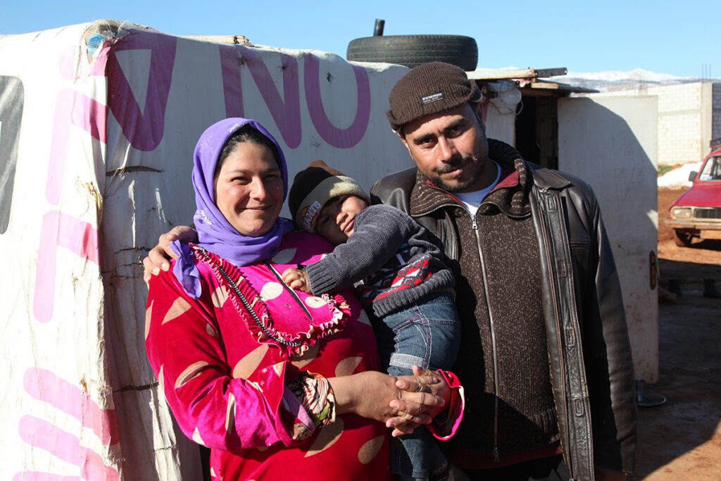 Esposo abraza mujer que carga hijo en campo de refugiados