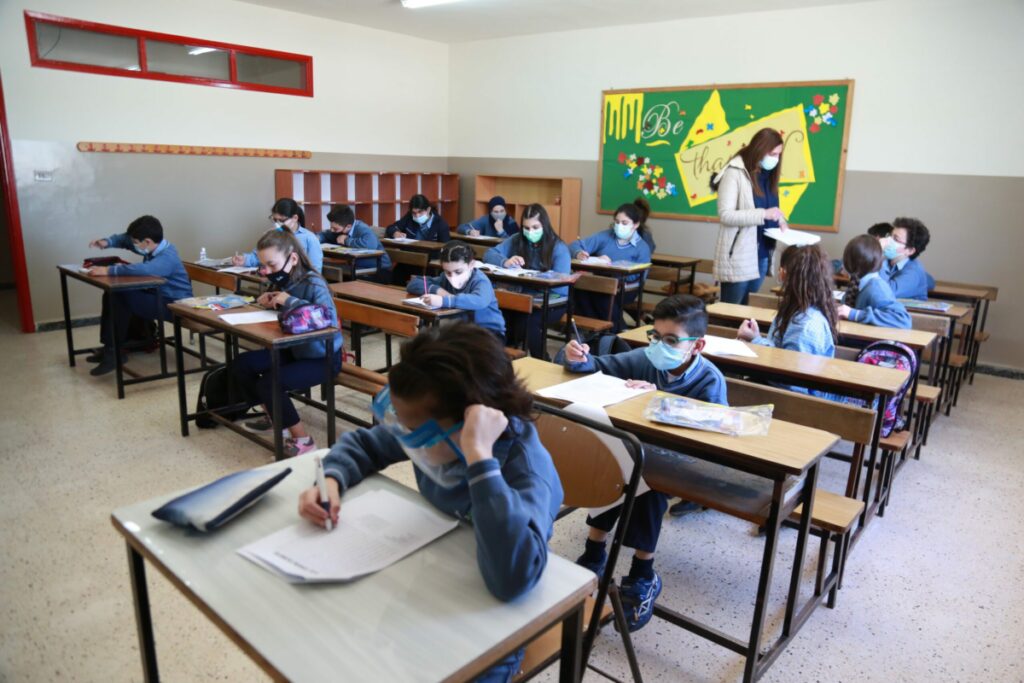 Niños estudiantes en uniformes azules trabajan en sus pupitres en un aula en la Escuela Nuestra Señora del Líbano en Rmeish, Líbano.
