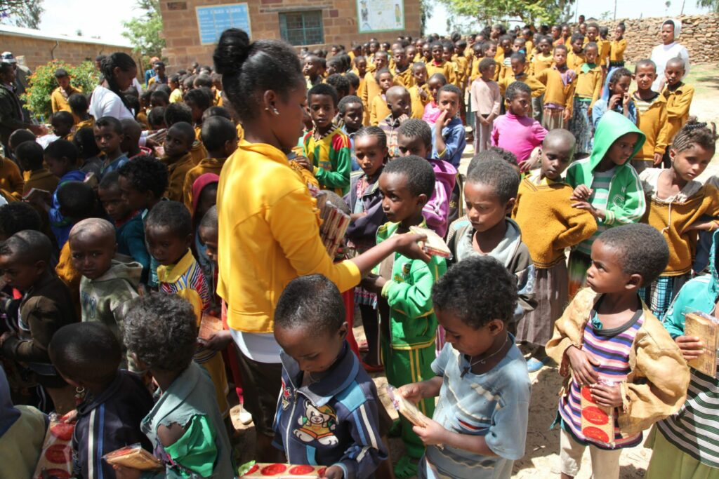 Una mujer con camisa amarilla distribuye comida a un gran grupo de niños en Etiopia