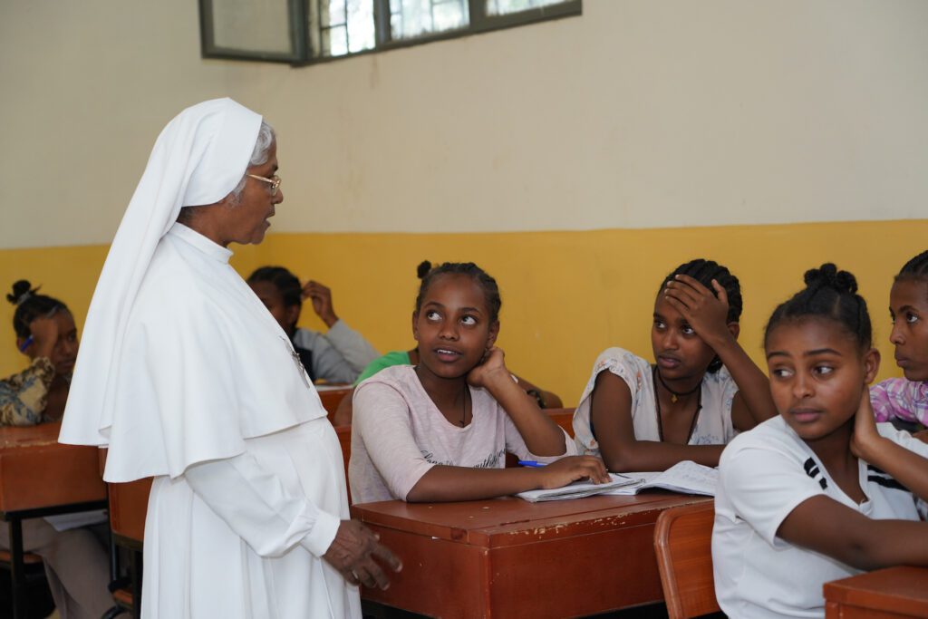 Religiosa con hábito blanco habla con niñas un una aula de un hogar para niñas en Etiopía.