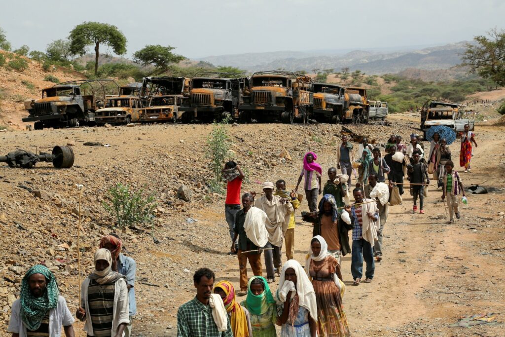 Un grupo de personas que regresan de un mercado en Tigray, pasan por un conjunto de vehículos quemados durante un sangriento conflicto.