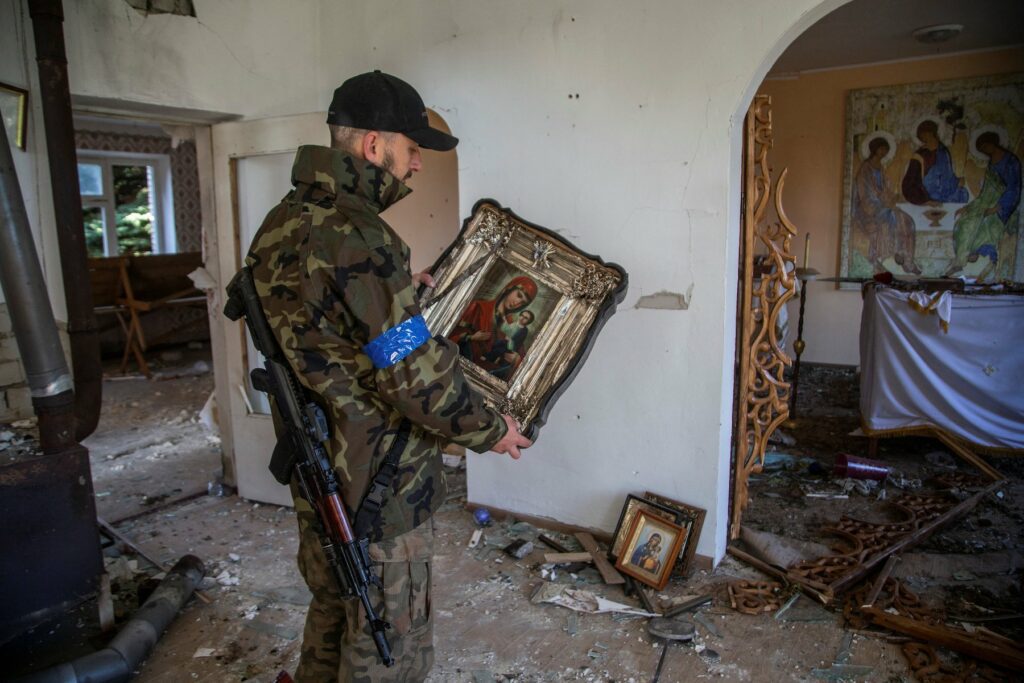 Militar ucraniano sostiene icono religioso dentro de iglesia destruída.