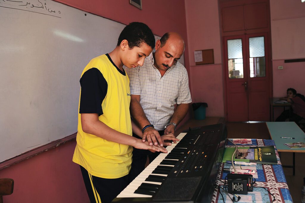 Profesor enseña a alumno a tocar el teclado en escuela de Egipto.