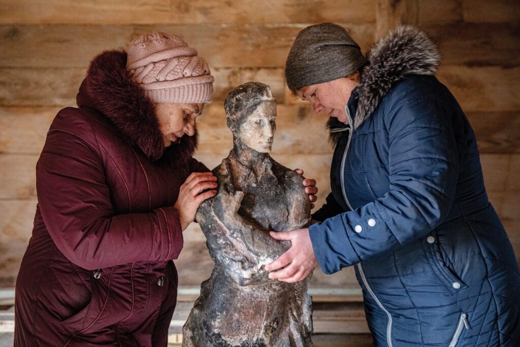 Dos mujeres sostienen una estatua dañada durante ataque ruso.
