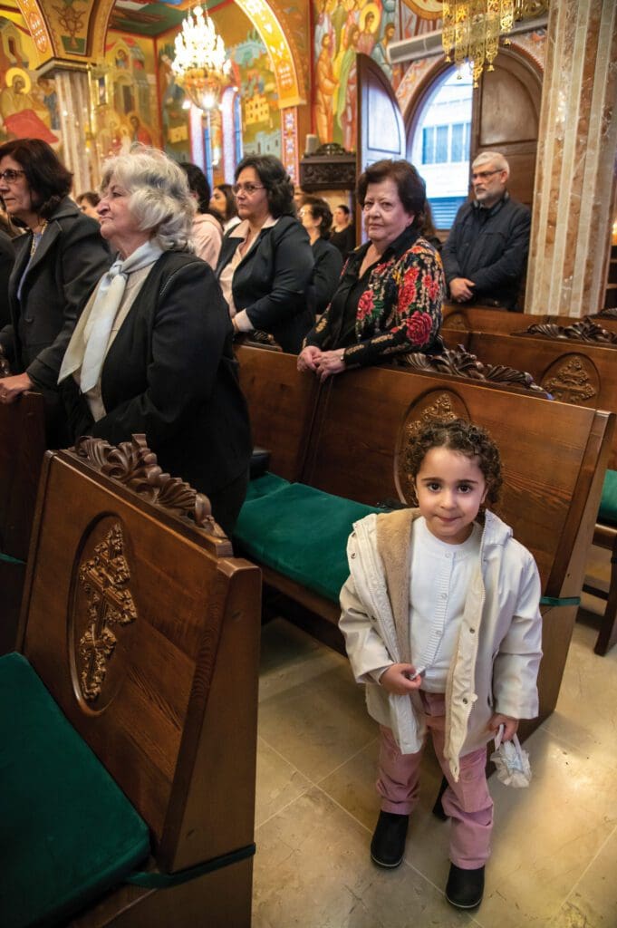 Ninna mira a la cámara en foto con feligreses parados en sus butacas en una iglesia.