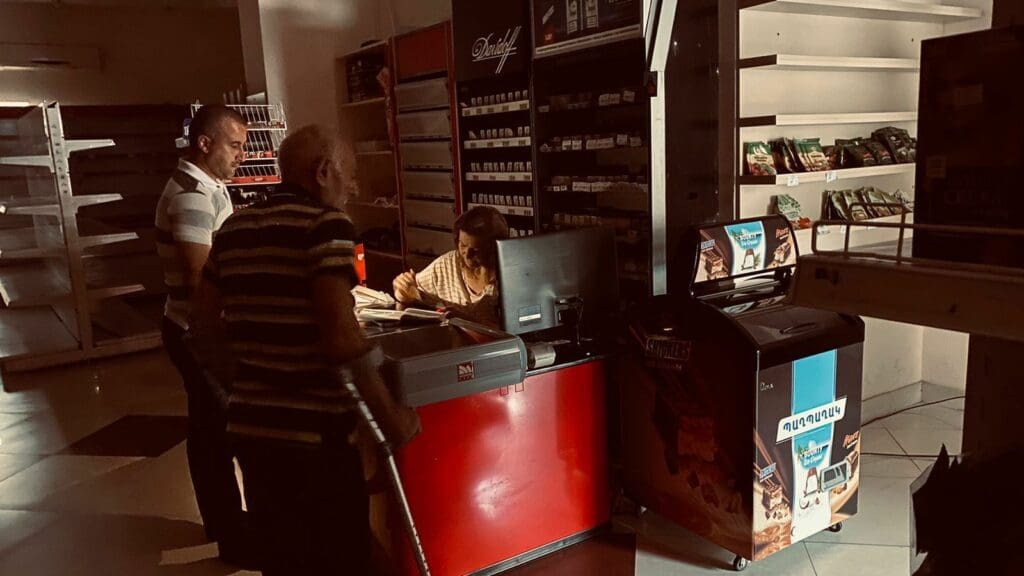 Dos hombres parados frente a una cajera sentada, en medio de un supermercado vacío.