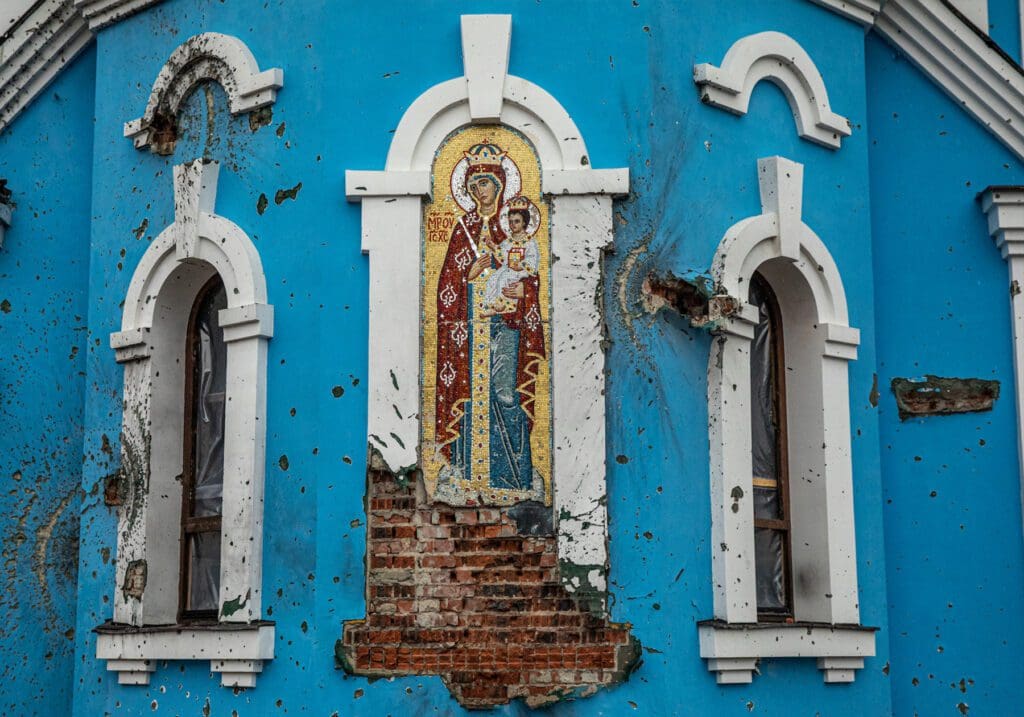 Un icono en mosaico de la Virgen María y Jesús está medio destruido, exponiendo los ladrillos del edificio debajo de él, en medio de otros daños causados por un bombardeo.