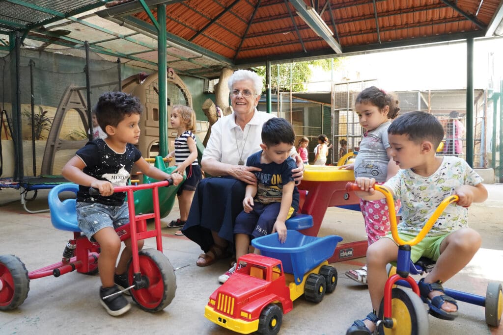 Religiosa de cabello cano juega con niños en guardería infantil.