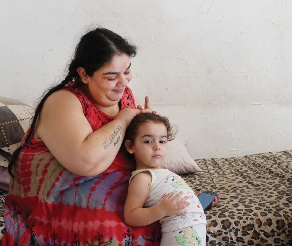 Madre sentada sobre una cama arregla el cabello de su pequeña hija.