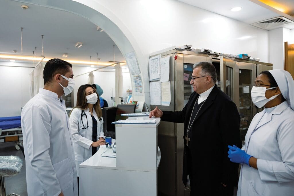 Sacerdote convers con personal médico en hospital en Irak.