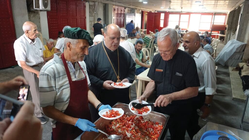 Dos sacerdotes y un hombre, sirven comida en un comedor para desplazados en Líbano.