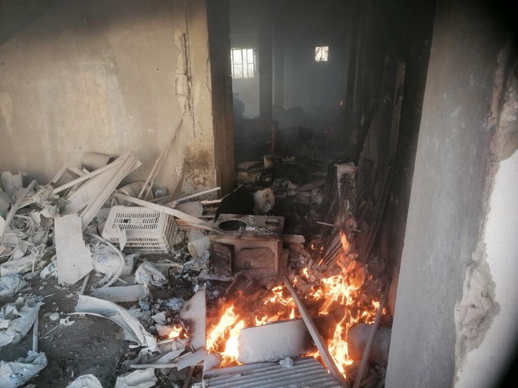 Habitación en ruinas con parte de los escombros en llamas.