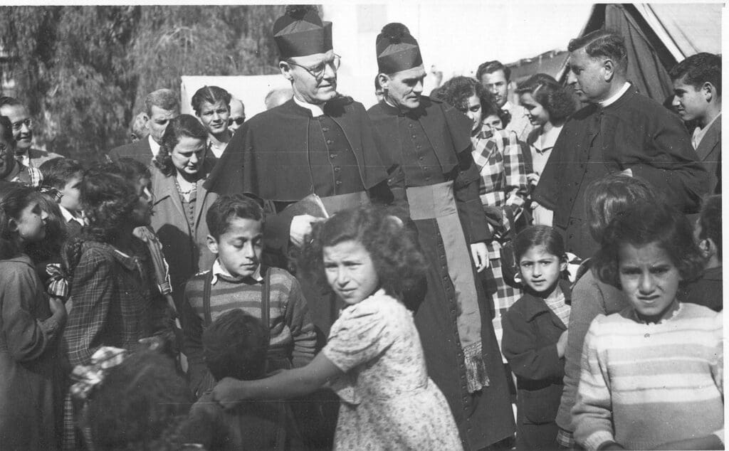 Foto de archivo en blanco y negro de tres sacerdotes en medio de una muchedumbre.