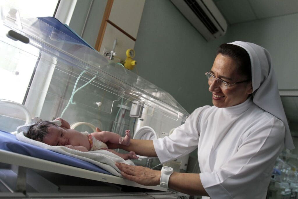 Una suora sorride a un neonato in incubatrice.