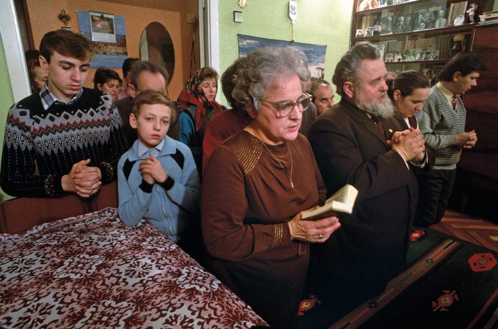 People of all ages stand in a small room praying.