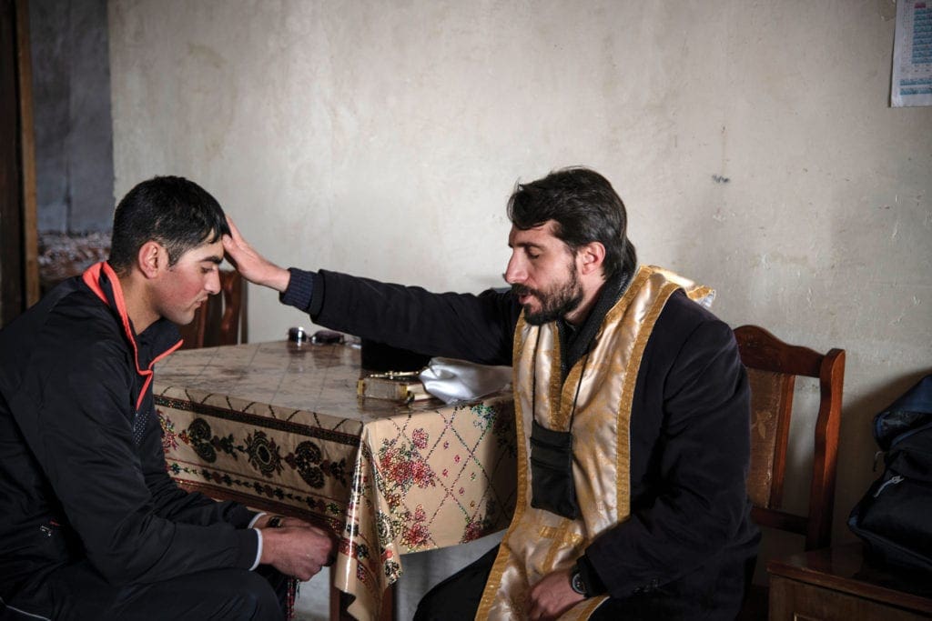 Priest places hand on a young man's forehead to bestow a blessing.