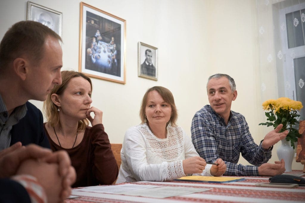 Several adult couples sit around a table, chatting.