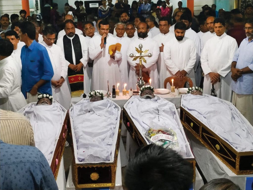 Clergy gather behind four open coffins at a large funeral liturgy.