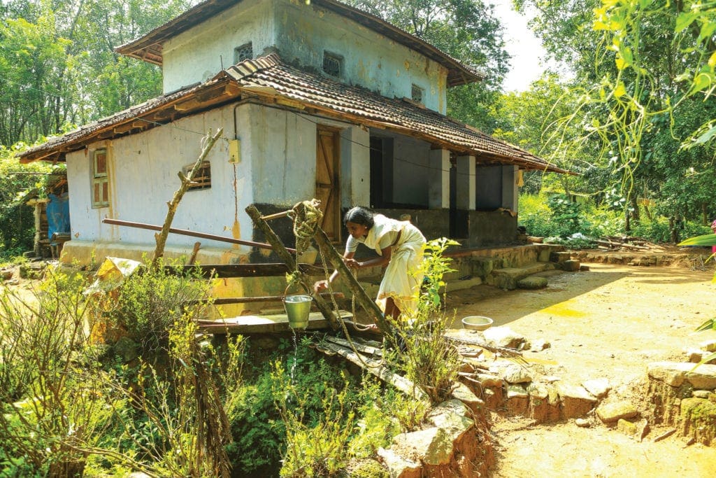 A woman draws water with a bucket and pulley outside of her house.