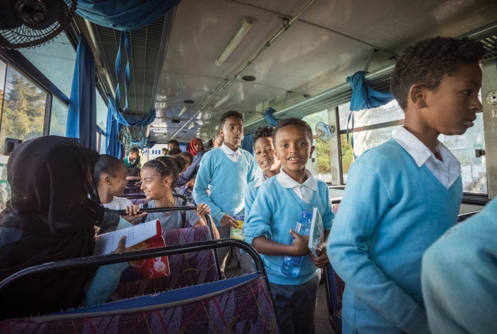 Grinning students walk down the center aisle of a bus.