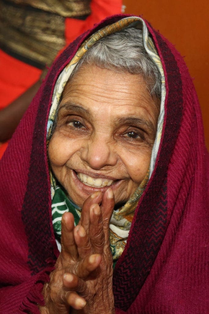an older woman wrapped in a shawl grins at the camera.