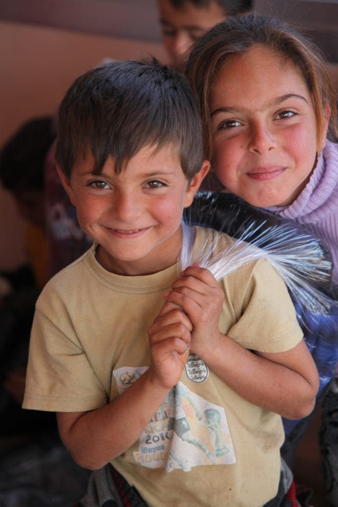 Two young children stand close together, grinning.