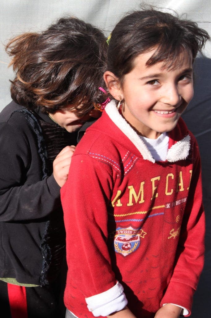 One young child grins at the camera while another, laughing, hides behind her.