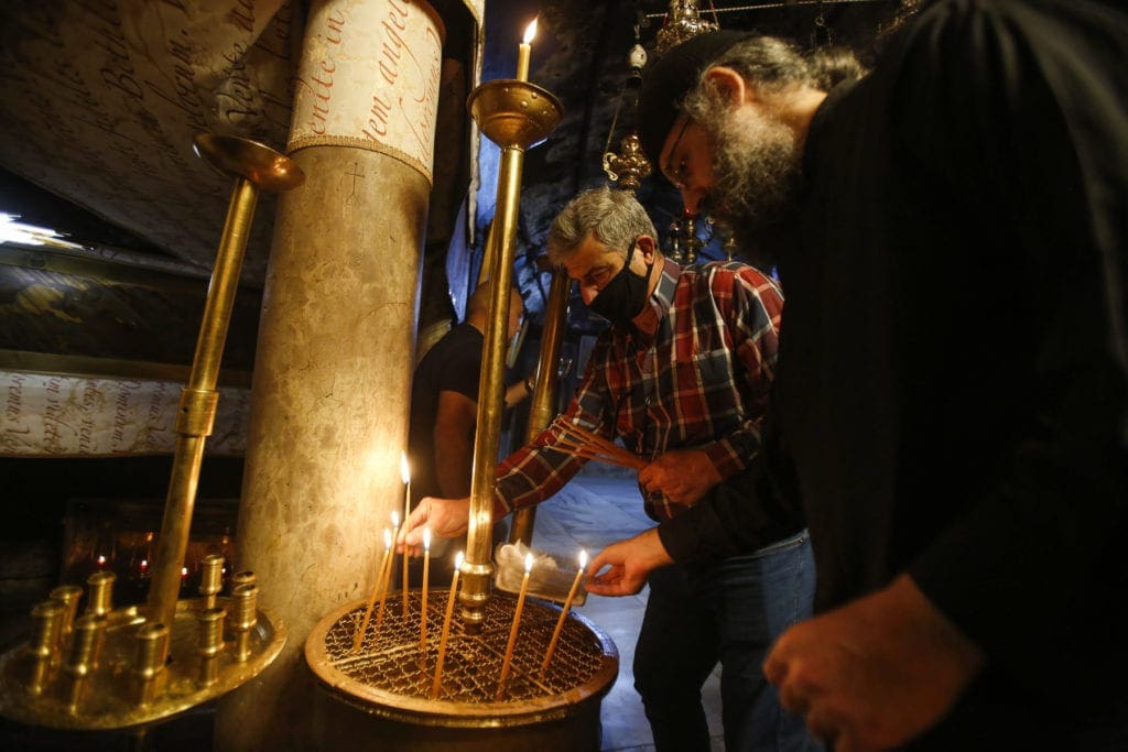 men light narrow candles beside a pillar in the Church of the Nativity.