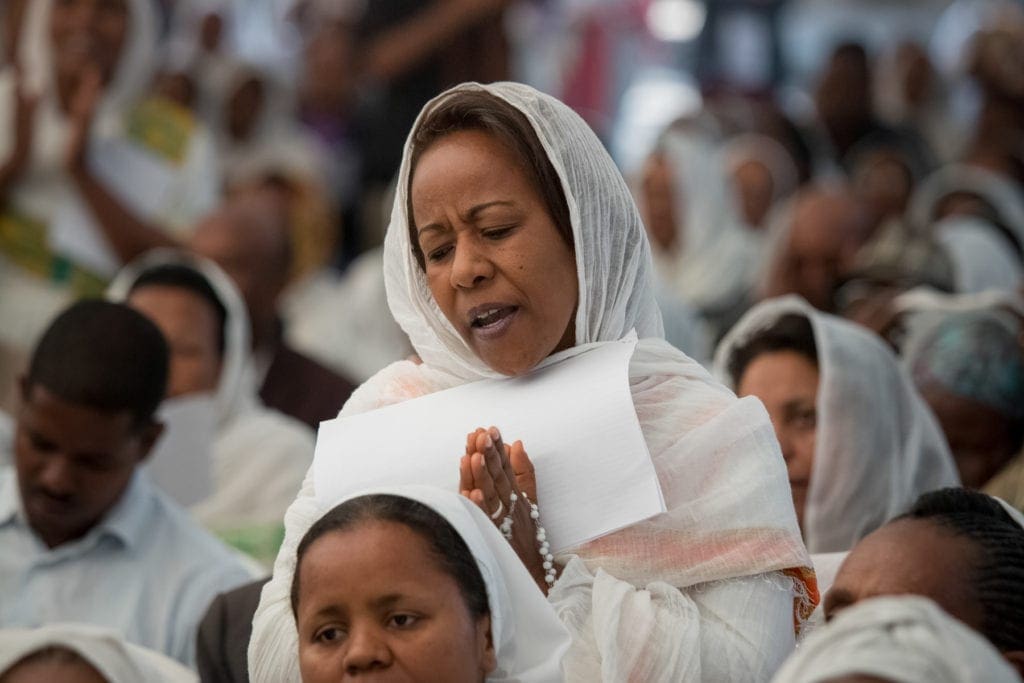 A woman prays in a crowd of parishioners wearing white.