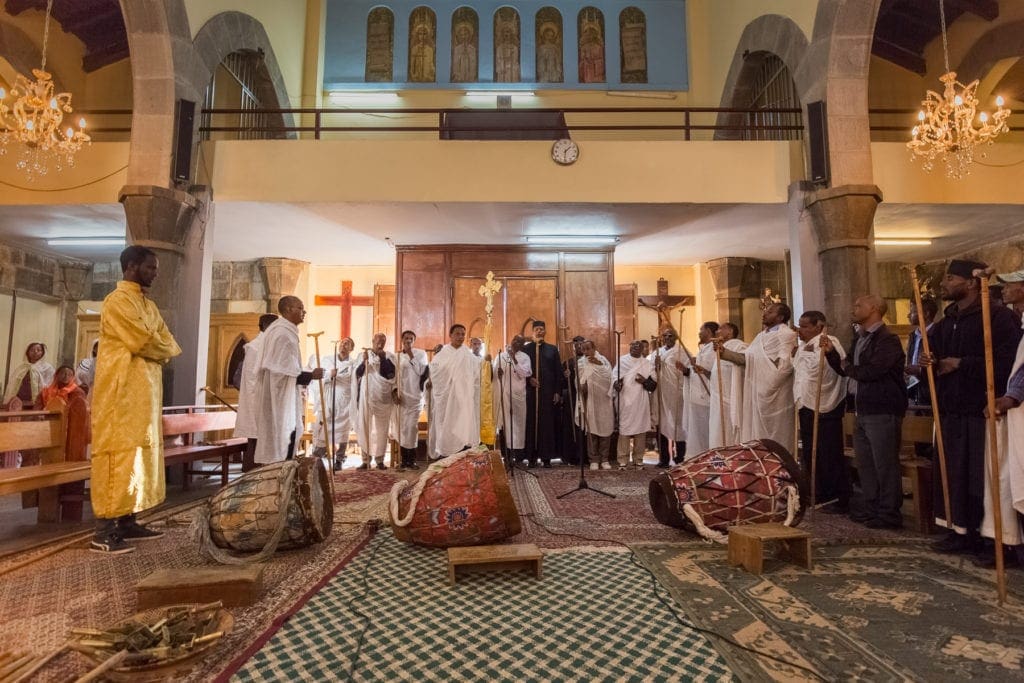 A gathering of clergy pray near several drums lying in the middle of a church.