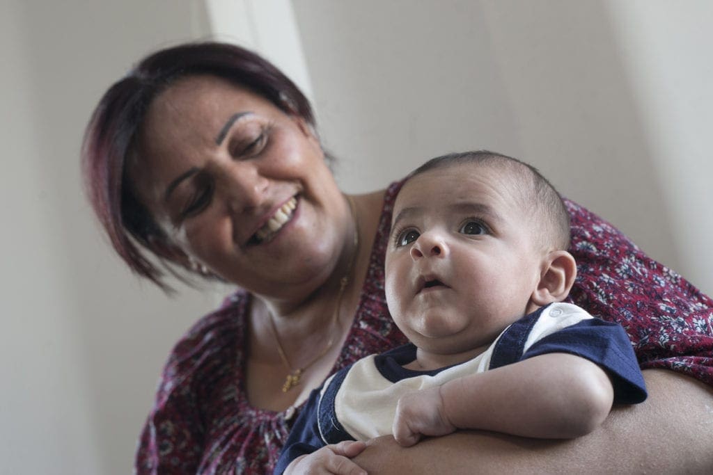 a woman grins at her infant grandson, who looks around with curiosity.