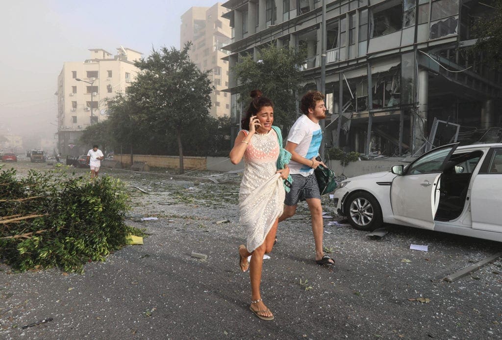 several people, including a woman speaking on her mobile phone, flee down a beirut street, smoke hanging in the air in the background.