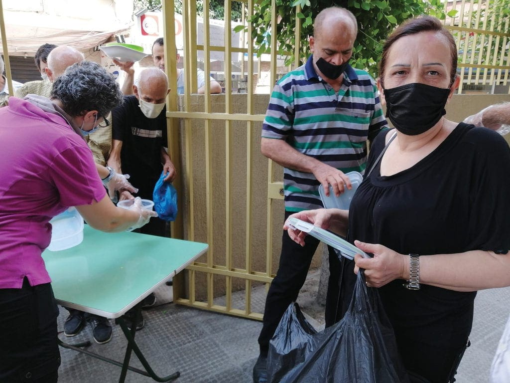 workers distribute food to locals at an outdoor table.