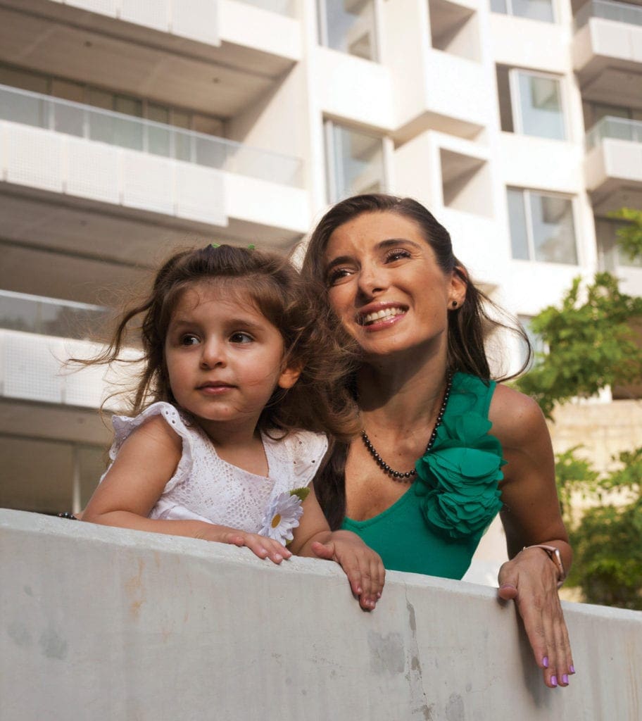 A woman and her young daughter look off at something out of frame from a small ledge.
