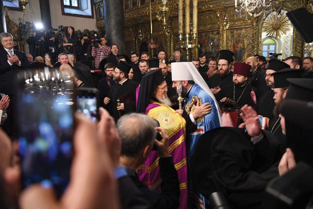 two church leaders embrace while the gathered crowd applauds.