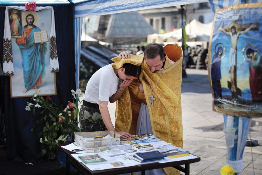 a priest blesses a woman outside near a tent canopy.