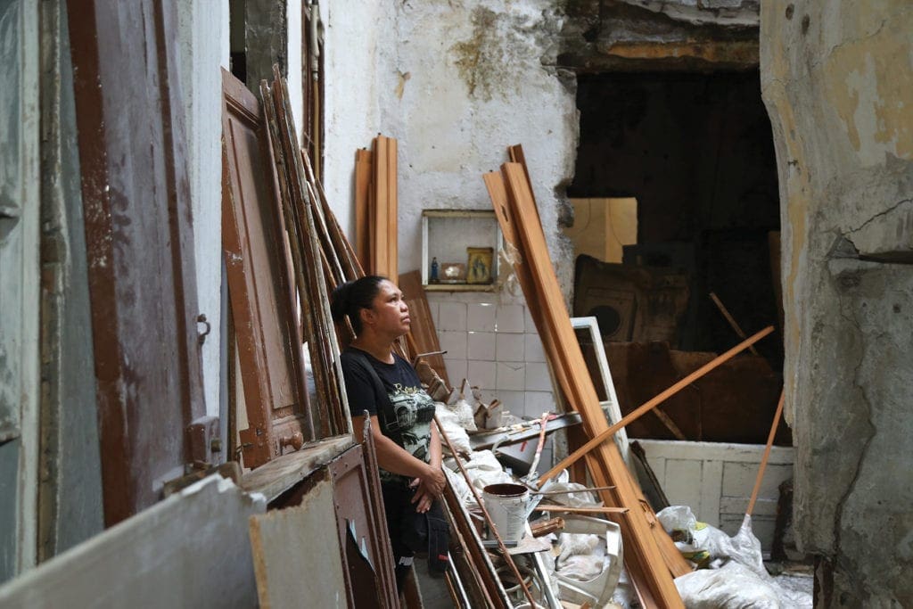 a woman stands near the rubble of her destroyed home.