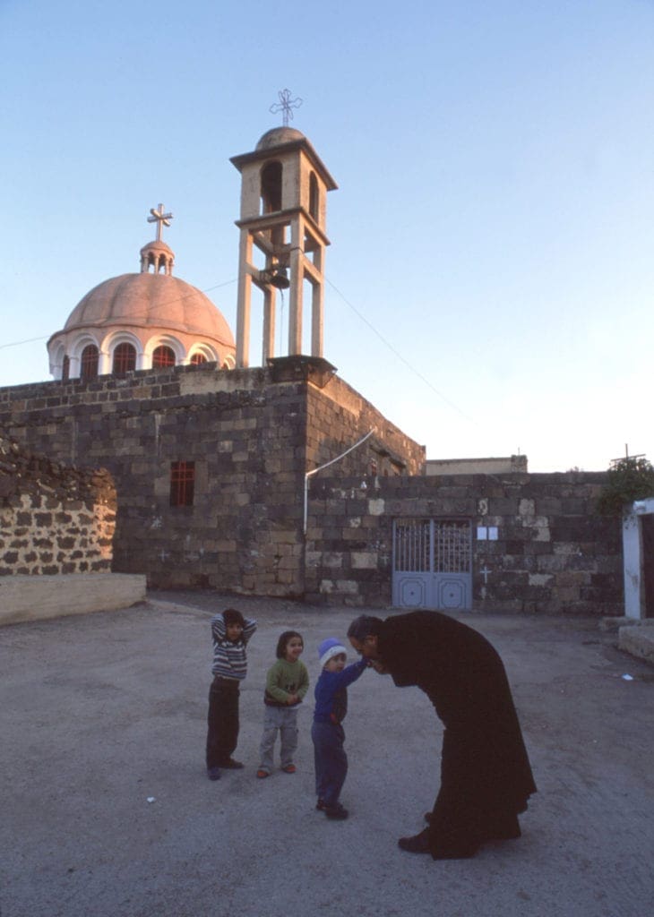 a priest greets three children outside of a church in the middle east.