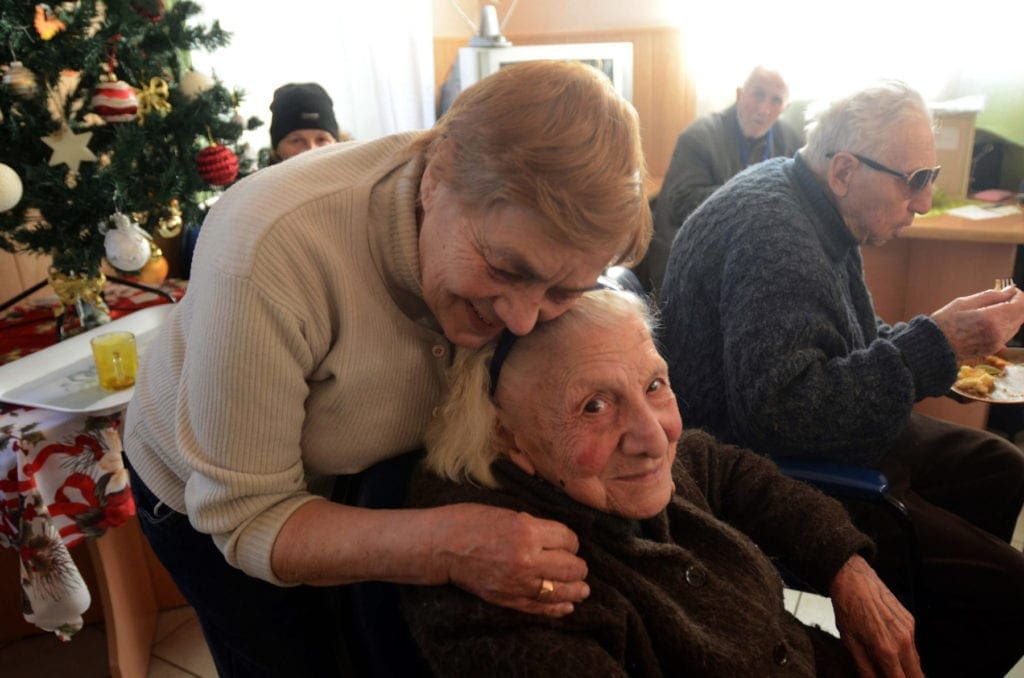 a woman embraces an elderly seated woman.
