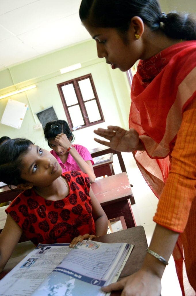 a young teacher helps a student at her desk.