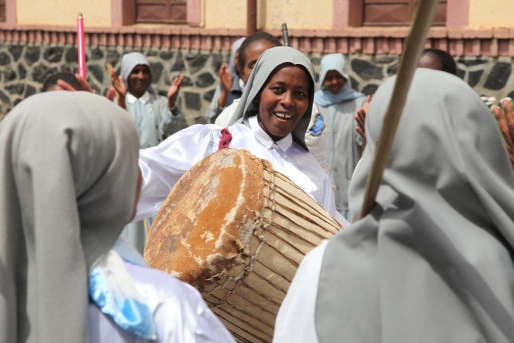 woman in veil playing a large drum outdoors in northeast africa.