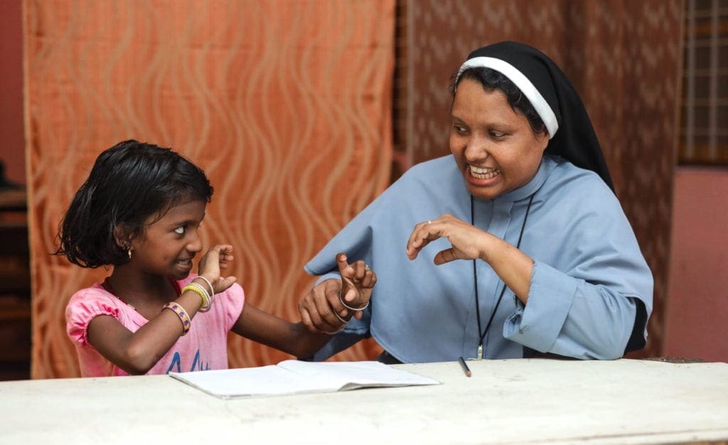 a nun and a young girl, seated at a table, pause from studying to play.