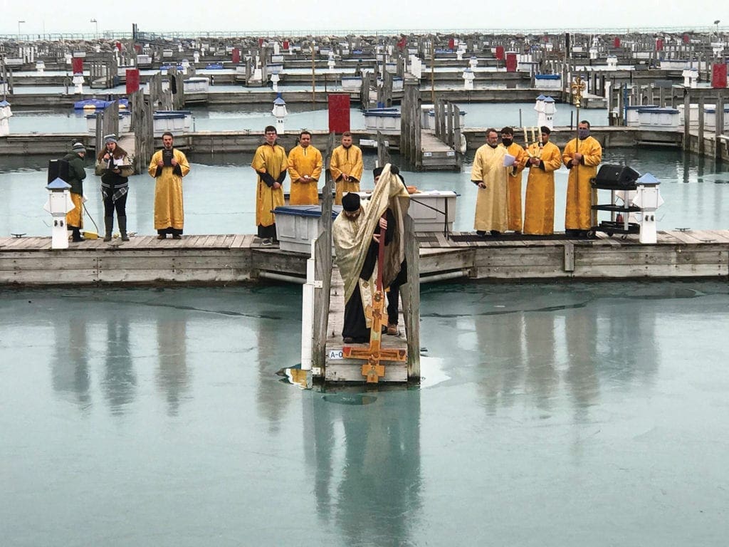 a priest dips a cross into Lake Michigan.