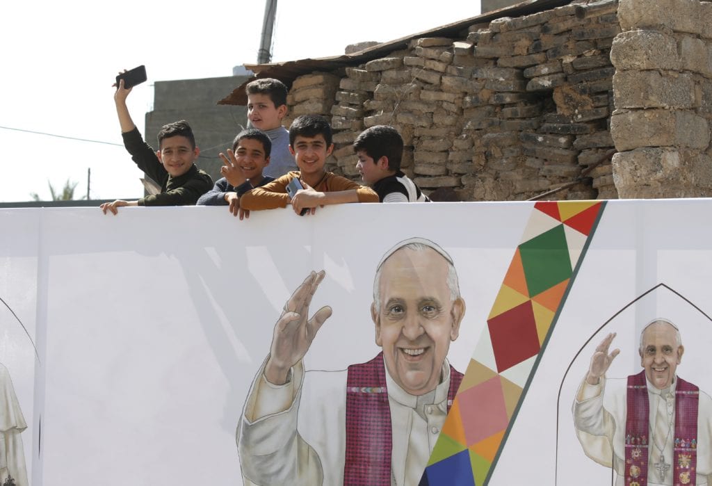 Children are seen near an image of Pope Francis during the pope's visit with the community at the Church of the Immaculate Conception in Qaraqosh, Iraq