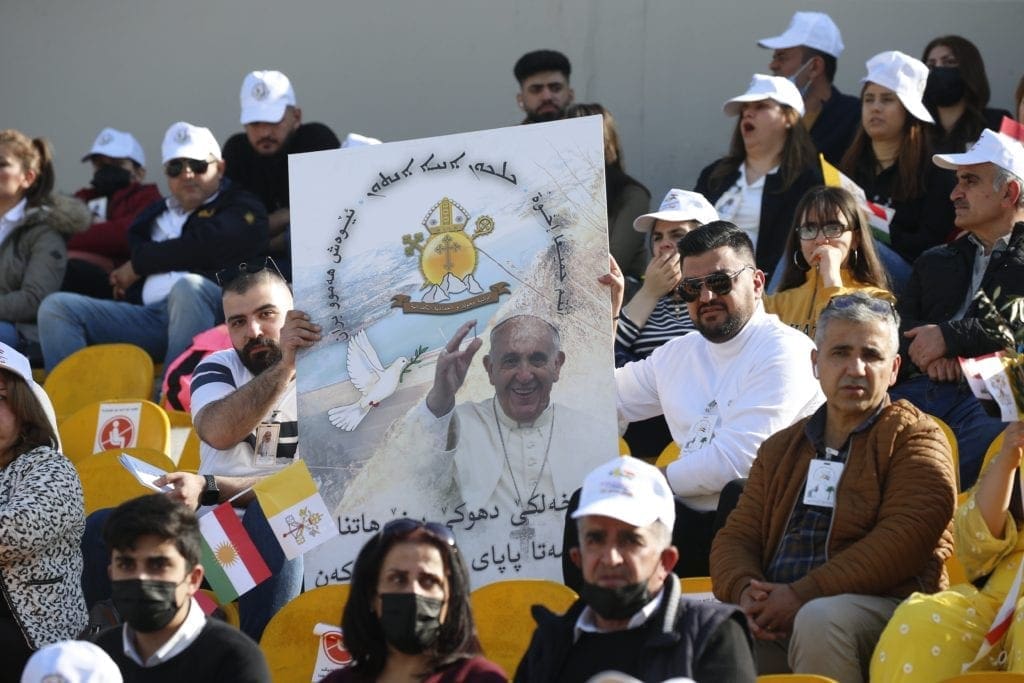 Men display a poster with an image of Pope Francis as the wait for him to celebrate Mass at Franso Hariri Stadium in Erbil, Iraq.