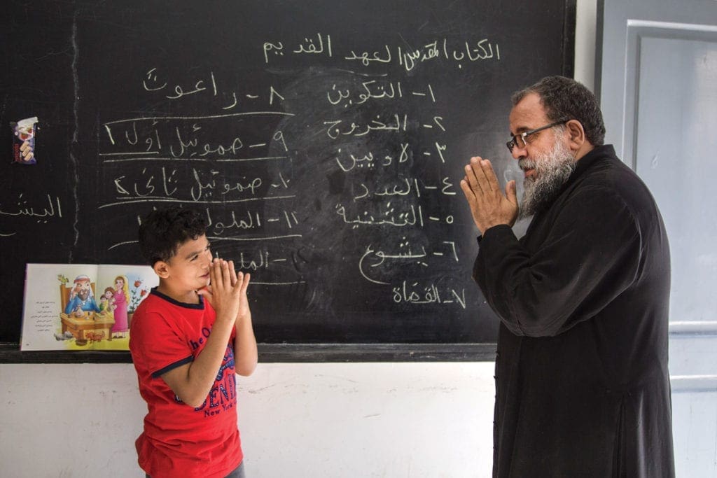 a priest delivers lessons in front of a chalkboard.