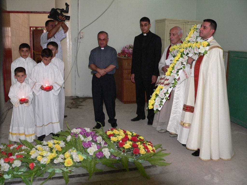 a priest holds a cross of flowers while praying.