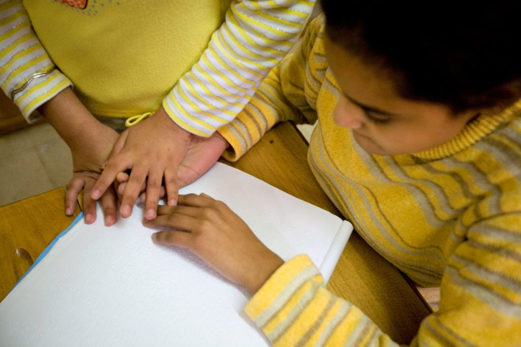 two children clasp hands at a desk in a home in Alexandria, Egypt..
