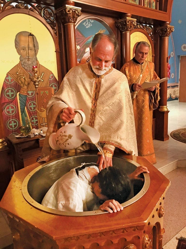 a priest baptizes a young parishioner.