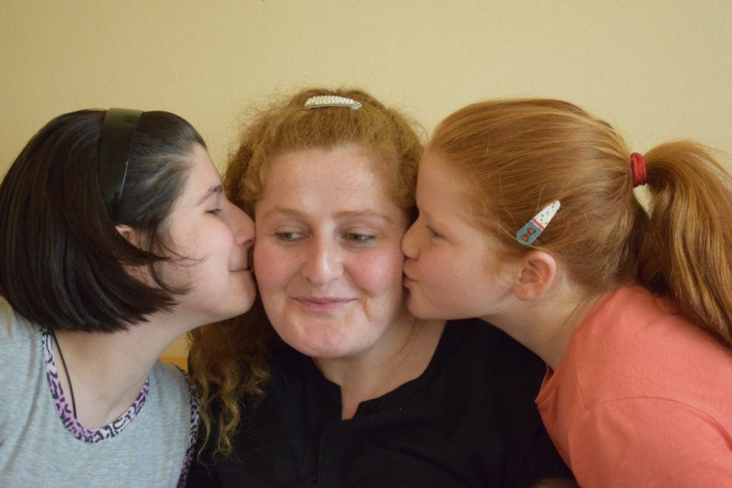two Georgian girls kiss their mother's cheeks.